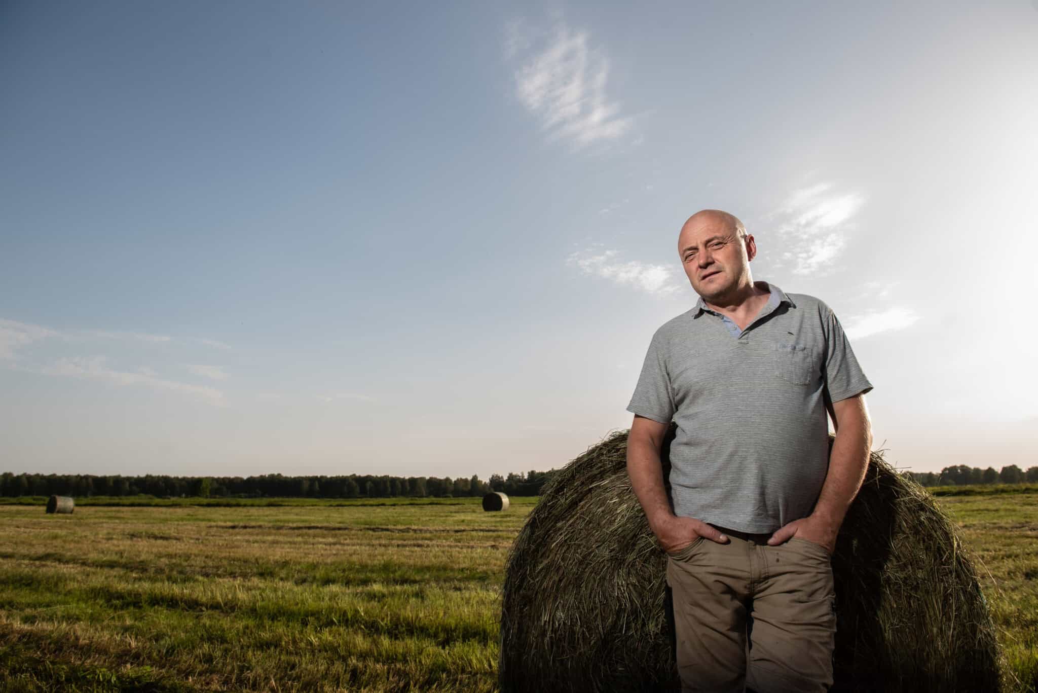 Jurijs standing beside a hay bale in a freshly mown meadow at Sita Nature Park